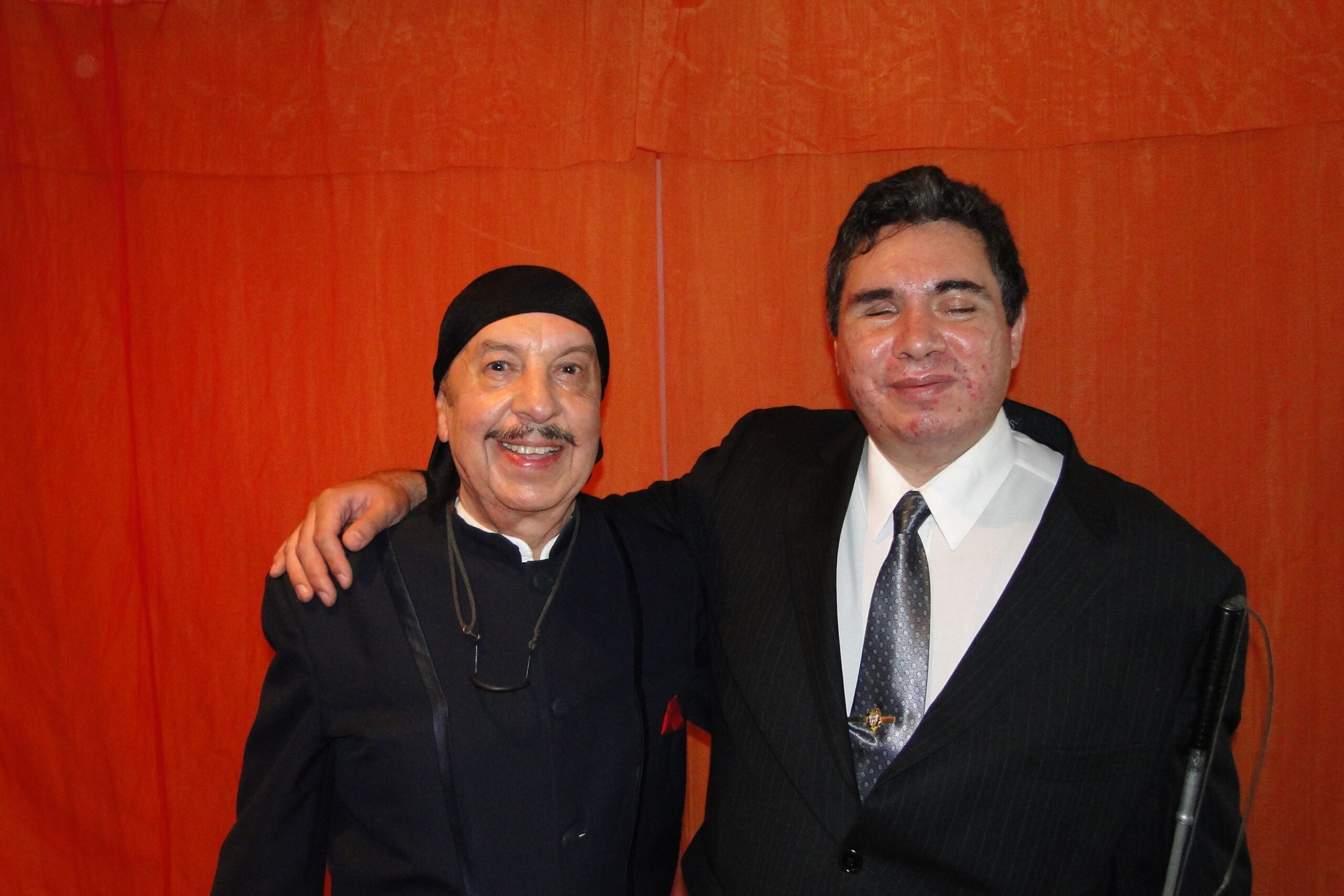 Fotografía de Eagleman junto al Mago Chen Kai frente a un fondo naranja, mostrando camaradería entre colegas.