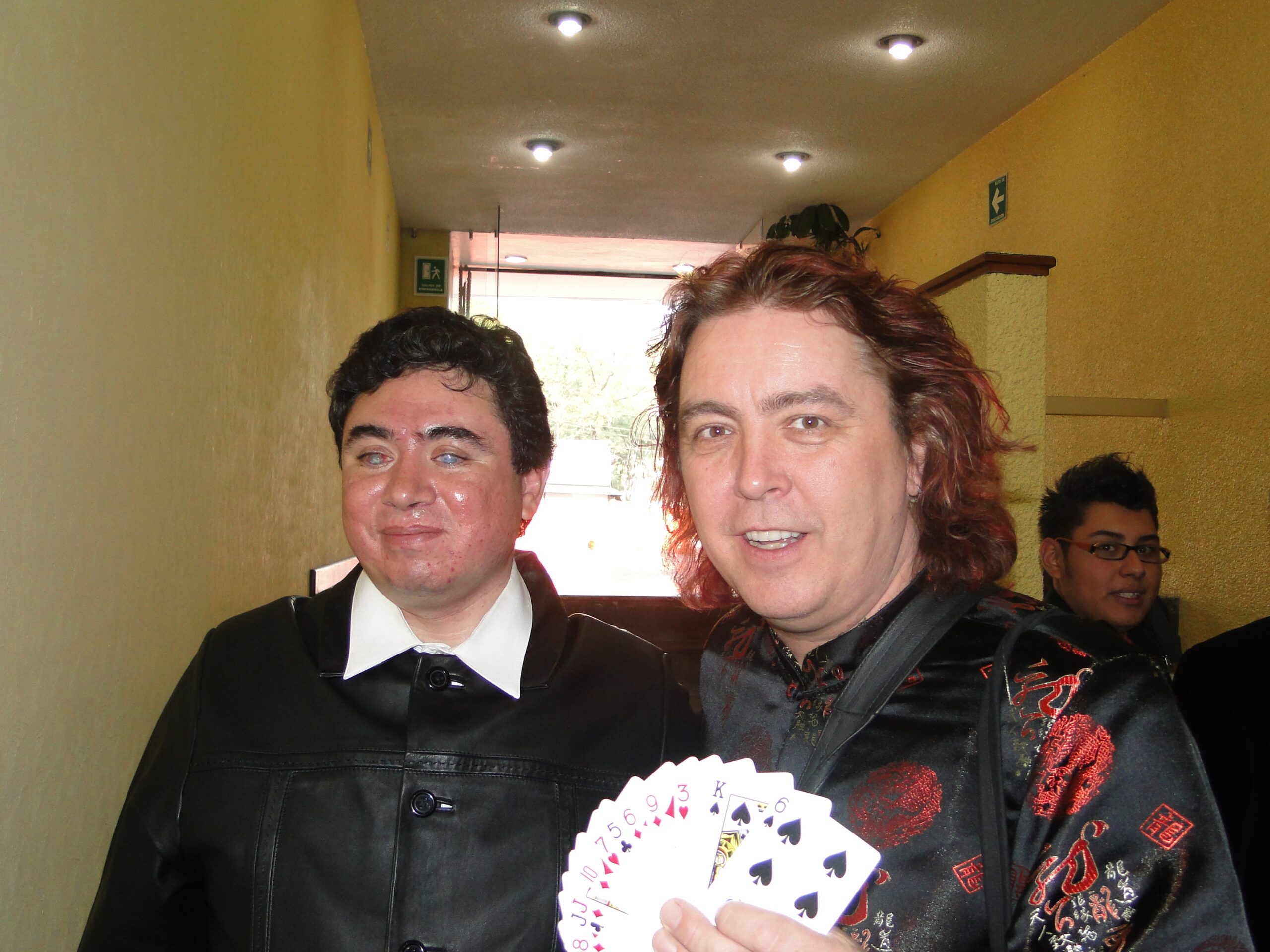 Fotografía de Eagleman junto al ilusionista estadounidense Jeff McBride, ambos vestidos de manera formal en un evento, con cartas de juego como parte de la presentación.