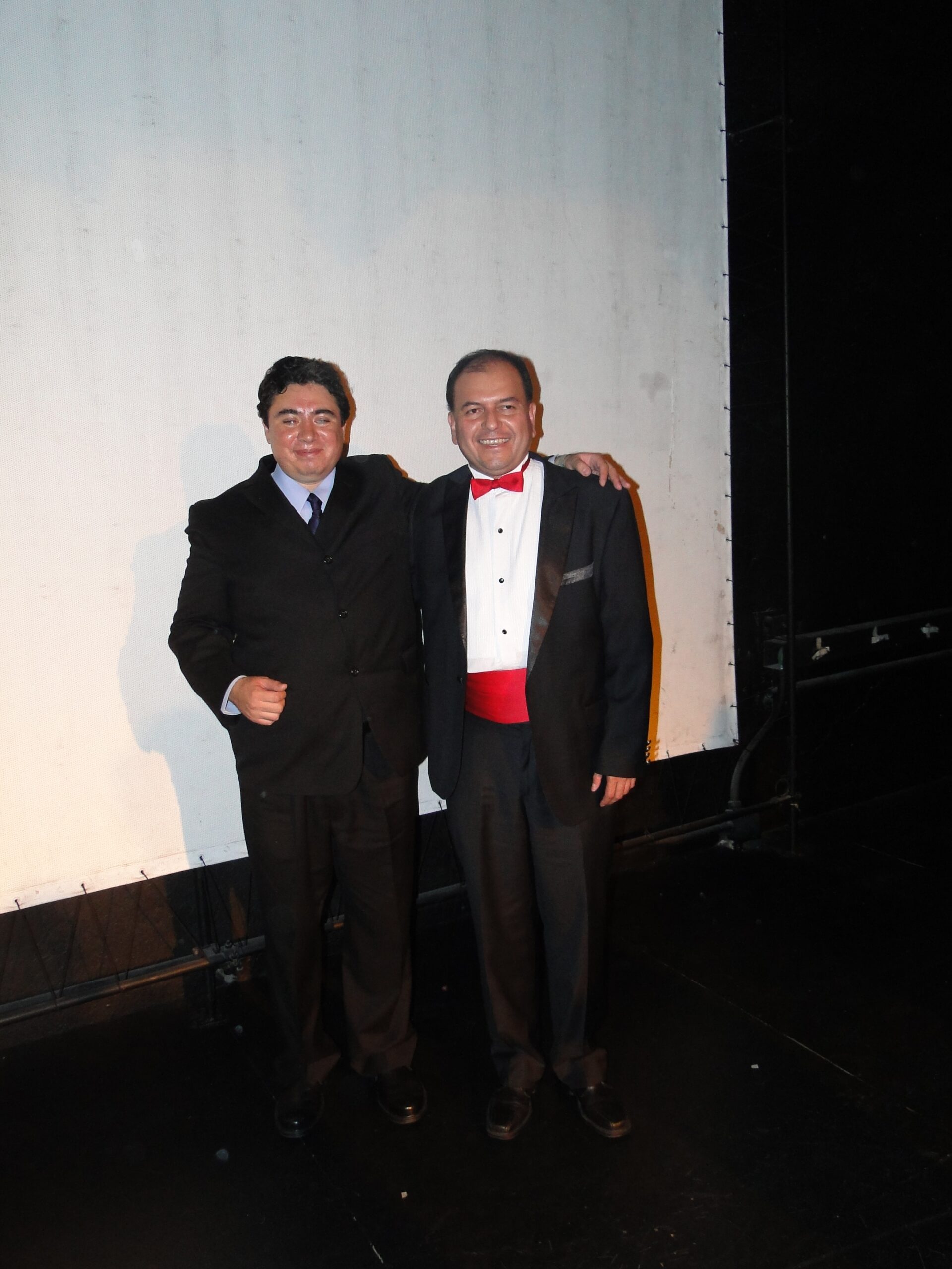 Fotografía de Eagleman junto al Mago Carlos Soriano en un evento formal, ambos vestidos de manera elegante sobre un escenario.