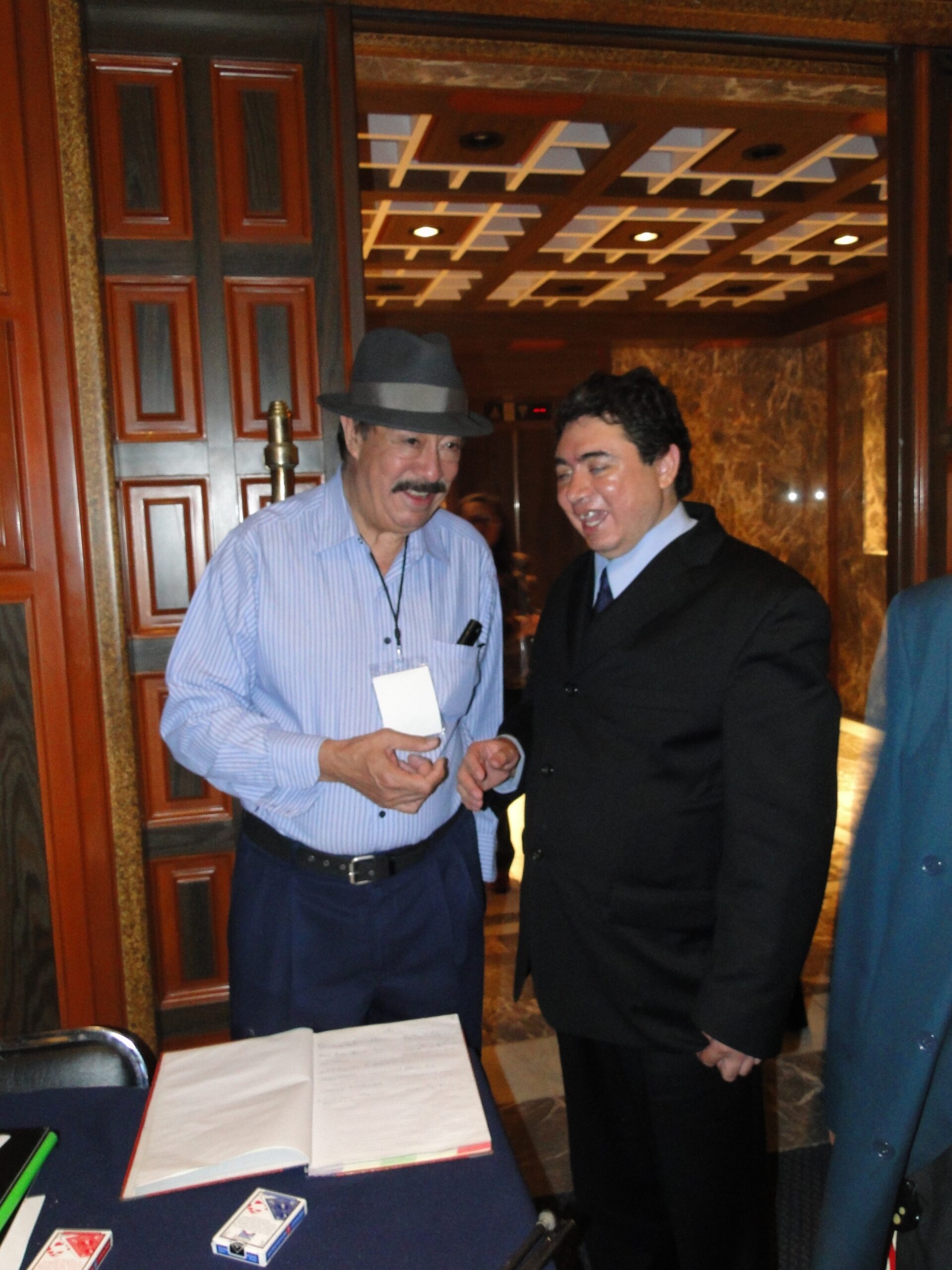 Fotografía de Eagleman junto al Mago Leonardo Trébole en un evento formal, con mesa y documentos al frente
